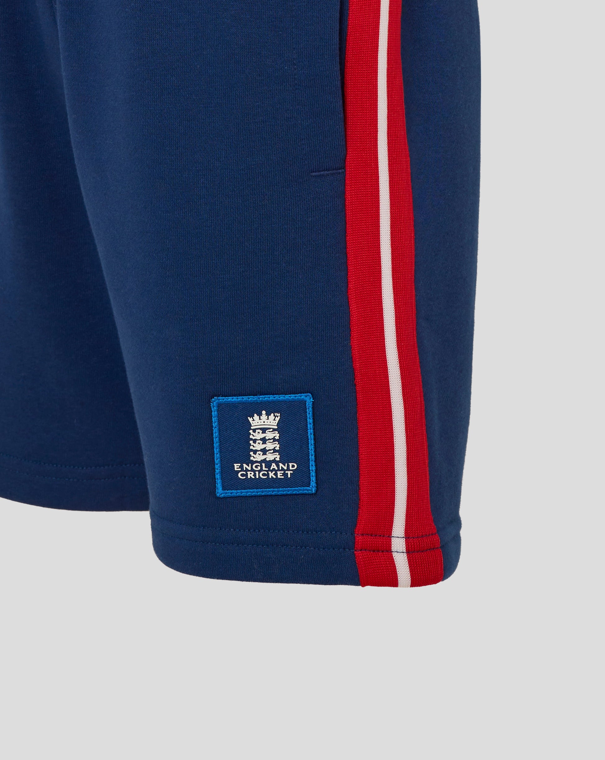 Close up of navy England Cricket Junior shorts showing red side stripe and blue crest patch