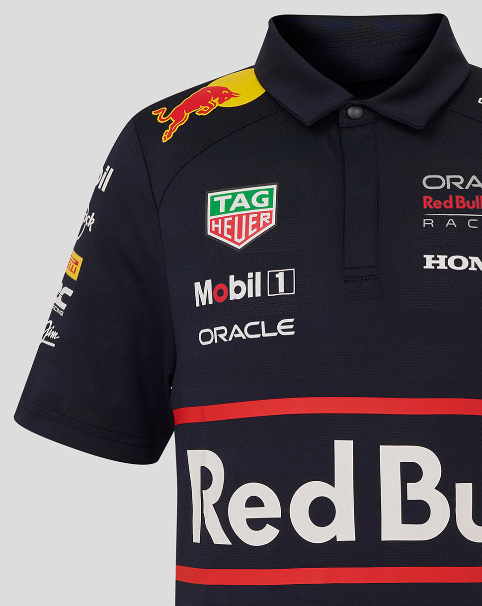 Upper front of navy junior polo with oversized Red Bull branding and multiple sponsor logos on the chest