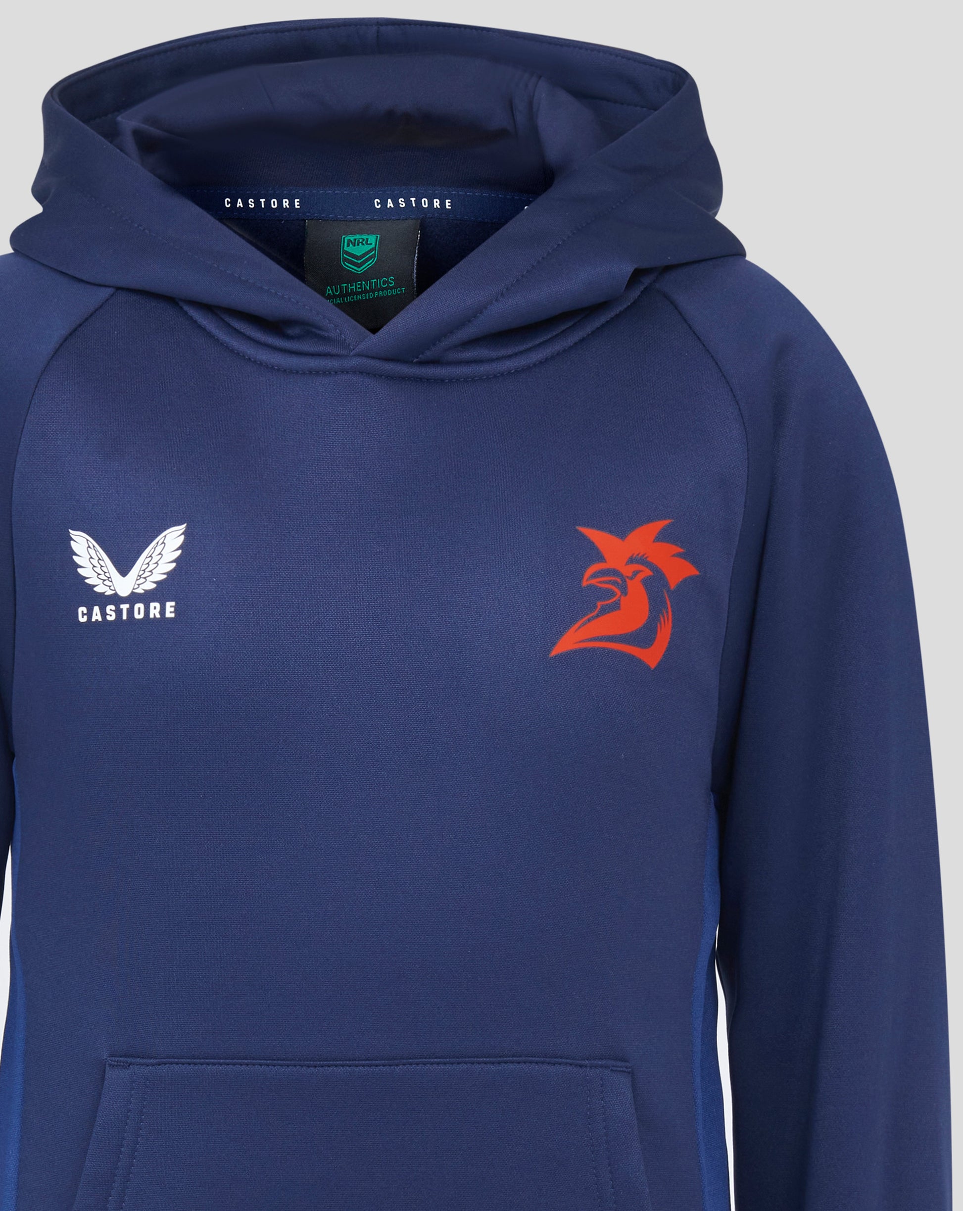 Front view of navy Sydney Roosters hoodie featuring white Castore logo on left chest and red rooster graphic; hood interior shows NRL Authentics label