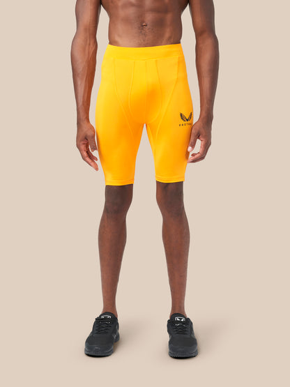 Front view of a man in bright zinnia orange base layer shorts with a logo on the thigh and black sneakers.