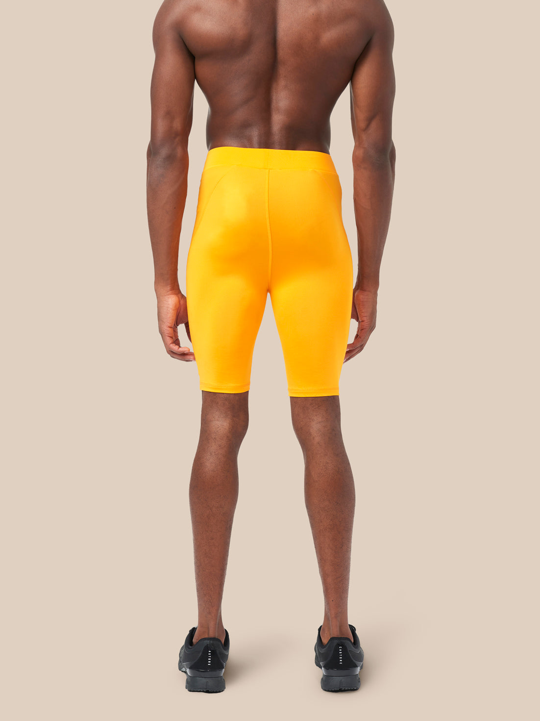 Back view of a male model wearing bright yellow Active Base Layer Shorts mid thigh length