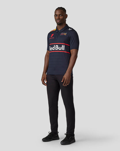 Full length view of a male model in a navy Oracle Red Bull Racing polo with a large Red Bull across the chest and branding