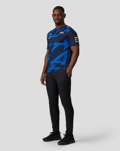 Full-length view of a man wearing navy BWT Alpine driver jersey with bold blue abstract graphics.