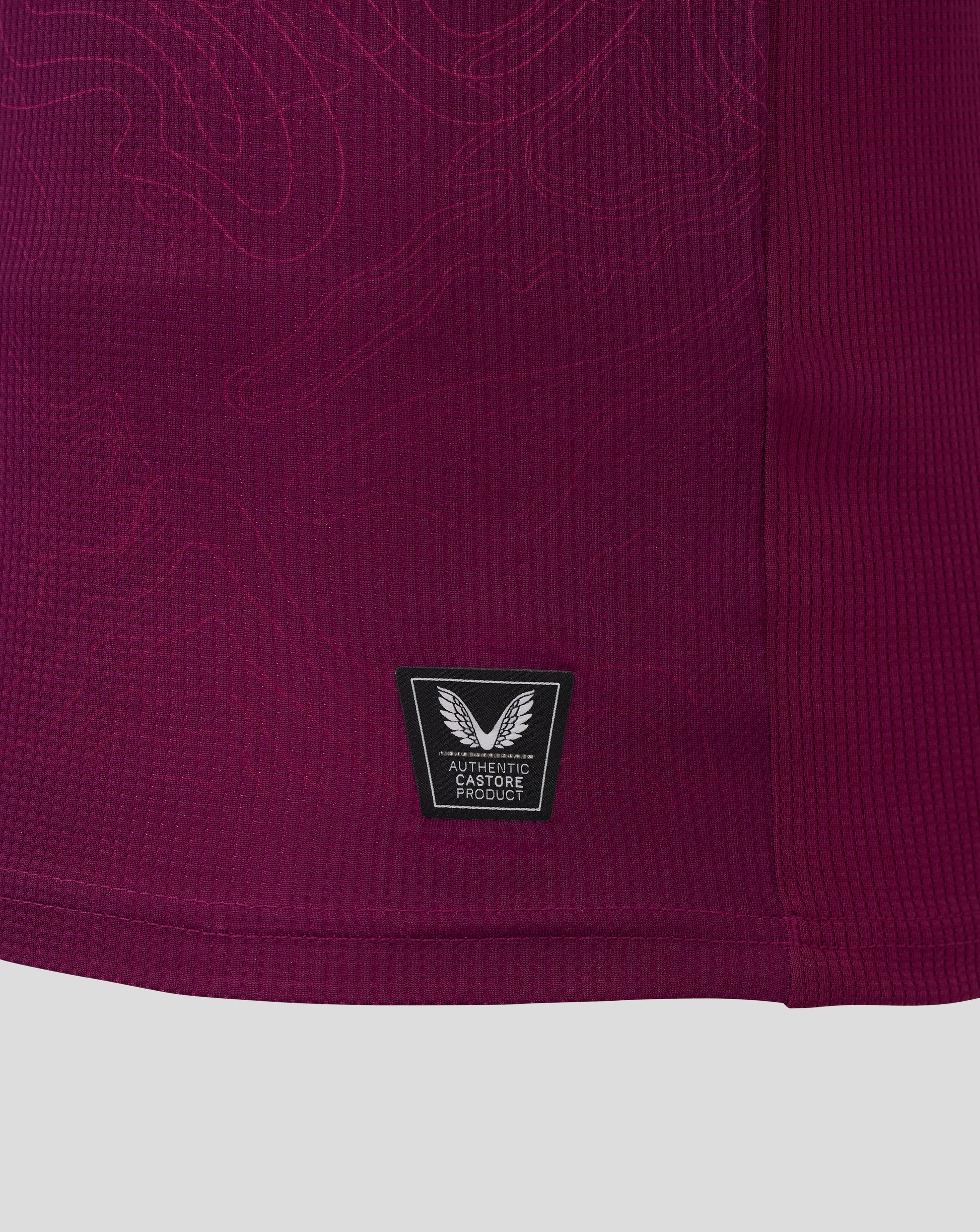 Close up of burgundy Burnley FC women's home shirt fabric with Castore authentic product badge.