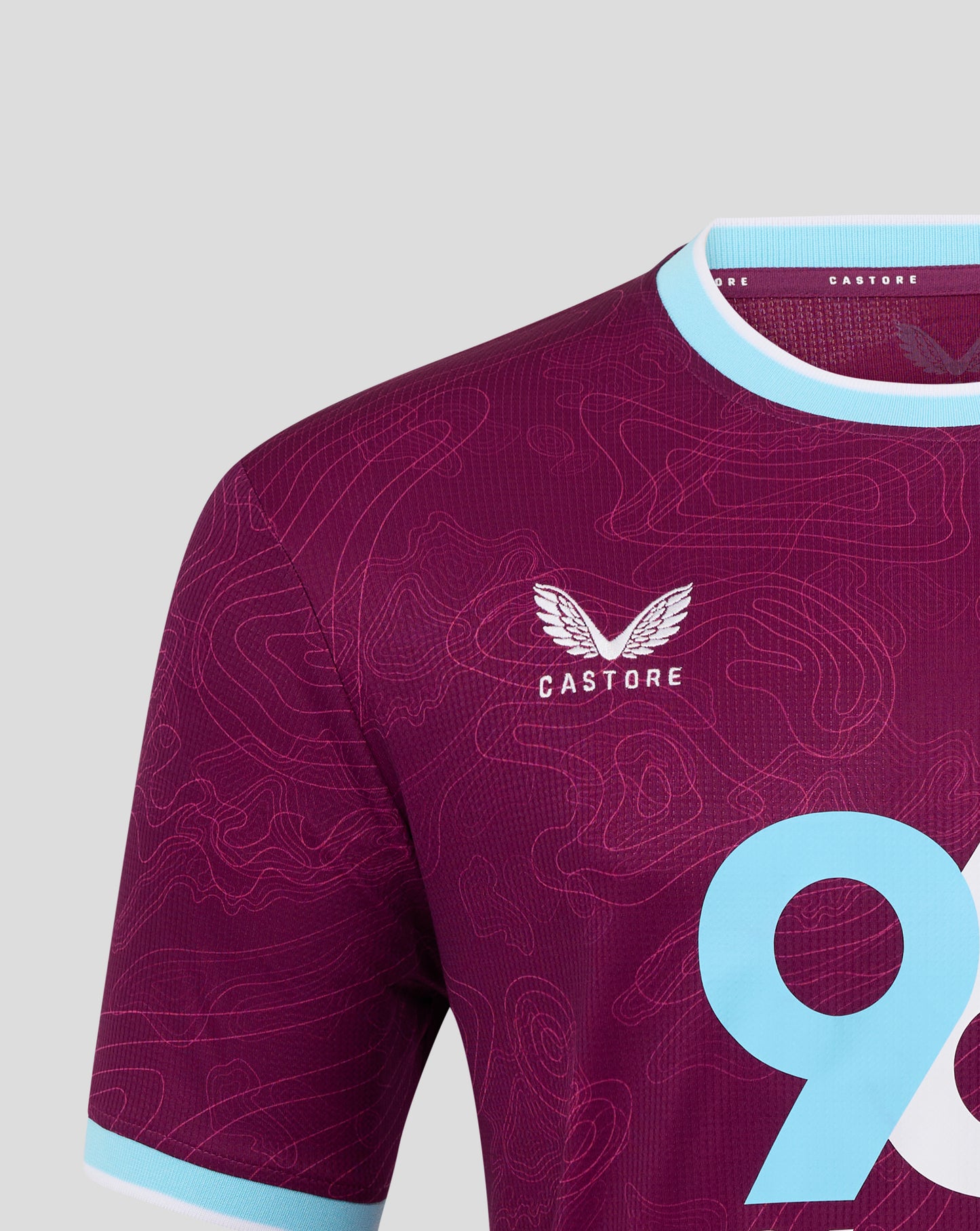 Close up of crest and pattern on burgundy Burnley shirt with light blue sleeve cuffs.