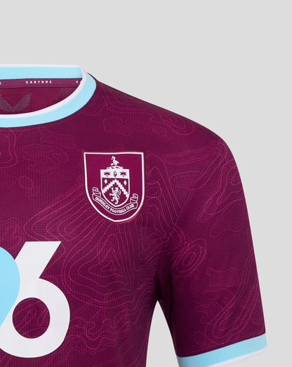 Close up of Burnley FC home shirt showing crest on burgundy fabric with pale blue neck trim.