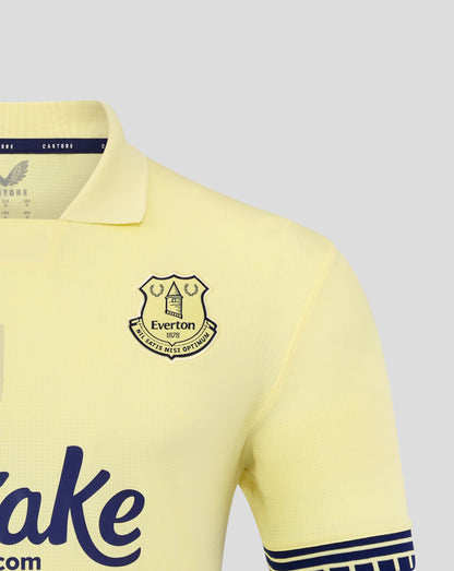 Close-up of pale yellow Everton FC away shirt showing crest on chest and navy collar trim.