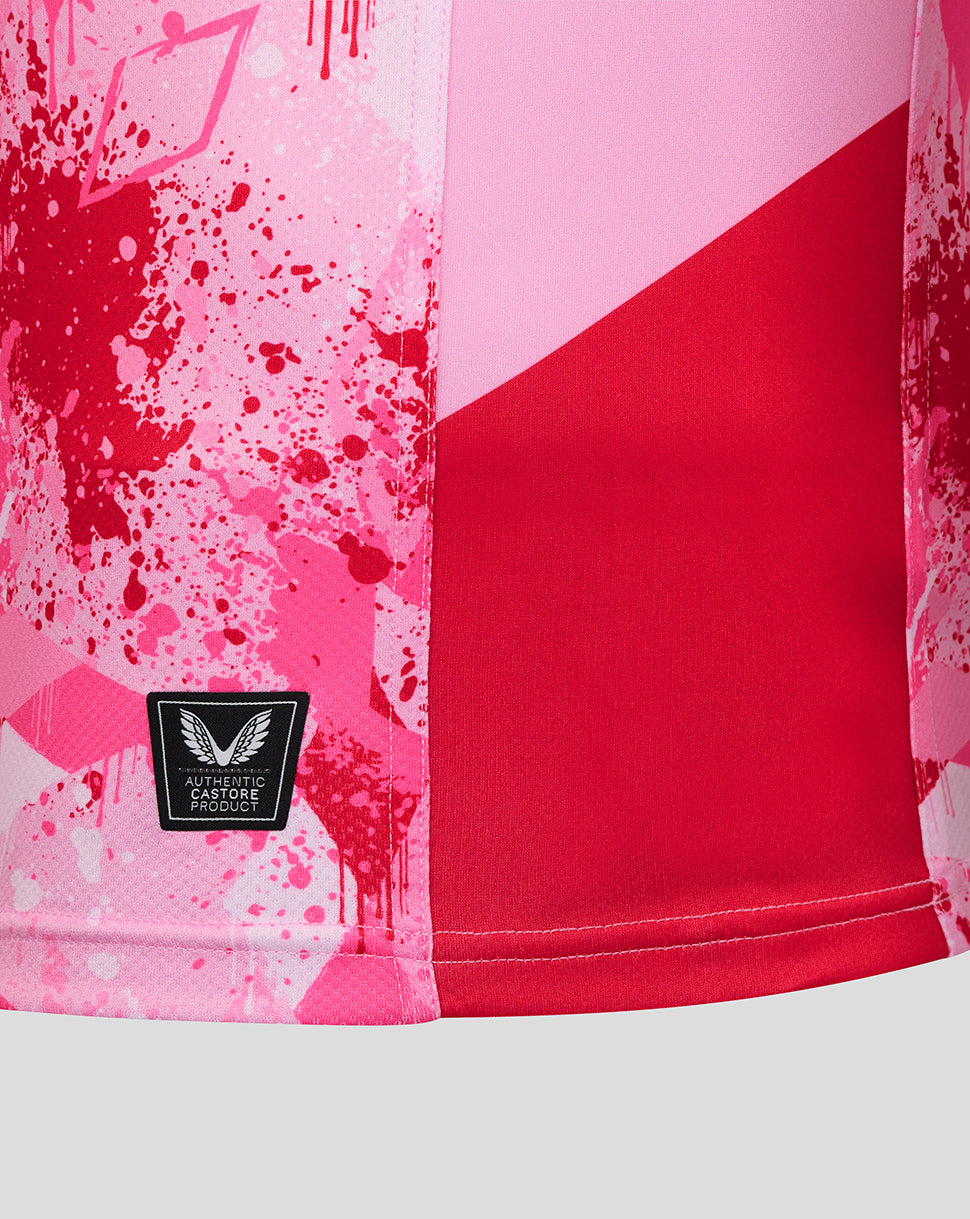 Close up of the shirt hem showing pink splatter print red panel and authentic Castore product patch