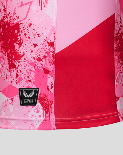 Close up of the shirt hem showing pink splatter print red panel and authentic Castore product patch
