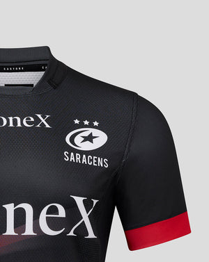 Close up of Saracens Pro Home Shirt chest showing crest, three stars, and oneX sponsor on black fabric with a red sleeve cuff