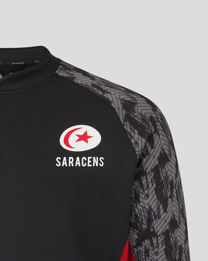 Close-up of the Saracens logo on a black drill top with grey patterned sleeves.