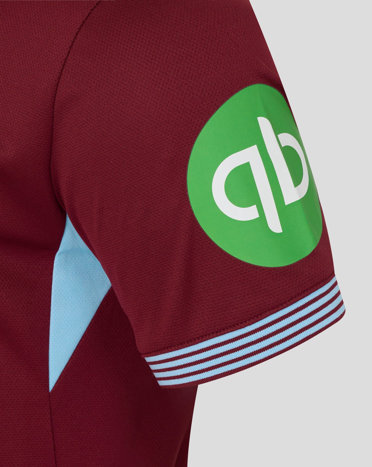 Close-up of burgundy West Ham home shirt sleeve with a bright green circular sponsor badge and light blue panel.