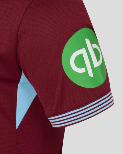Close-up of burgundy West Ham home shirt sleeve with a bright green circular sponsor badge and light blue panel.
