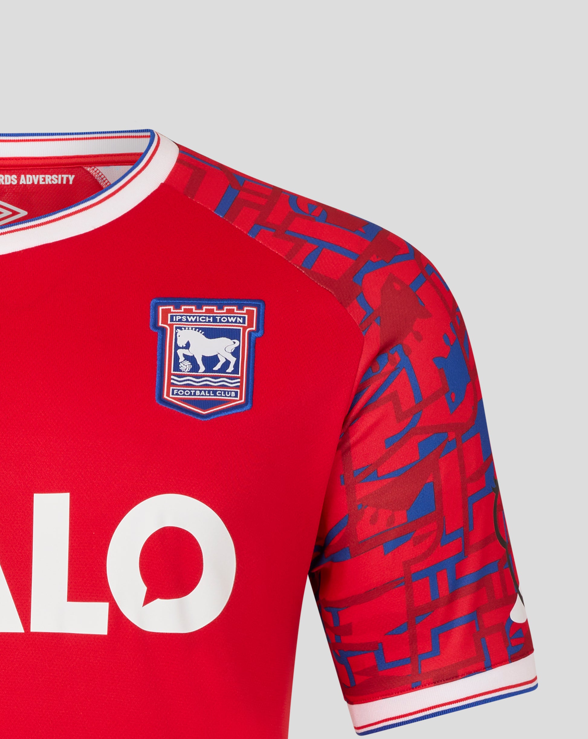 Close up of shoulder showing red away jersey with blue geometric sleeve pattern and white trim