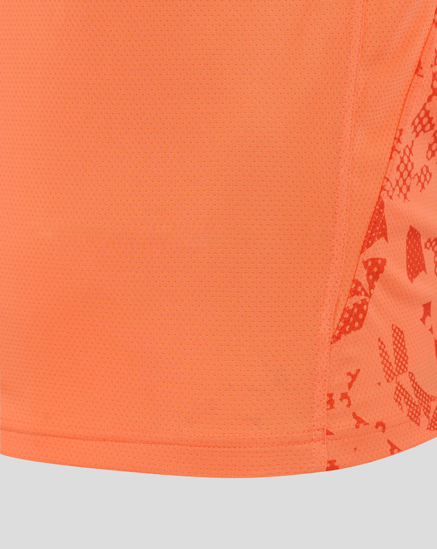 Close-up of bright melon mesh fabric from the England Rugby performance shirt, showing tiny perforations and a curved hem with partial side print
