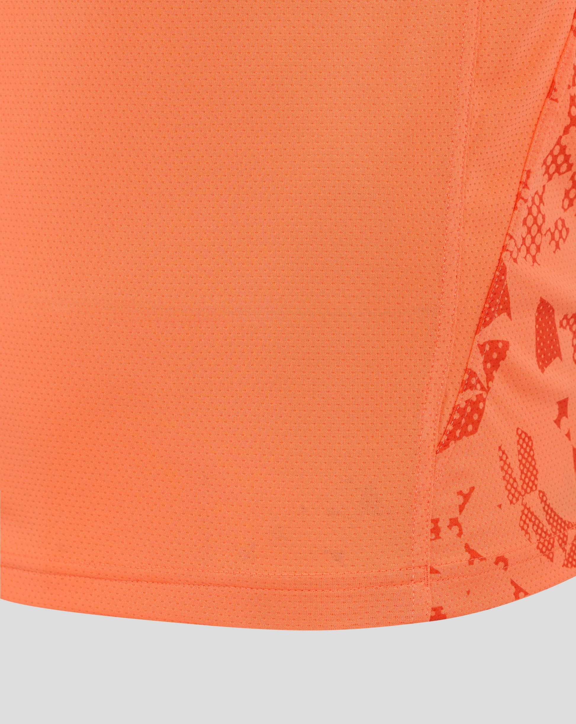 Close-up of bright melon mesh fabric from the England Rugby performance shirt, showing tiny perforations and a curved hem with partial side print