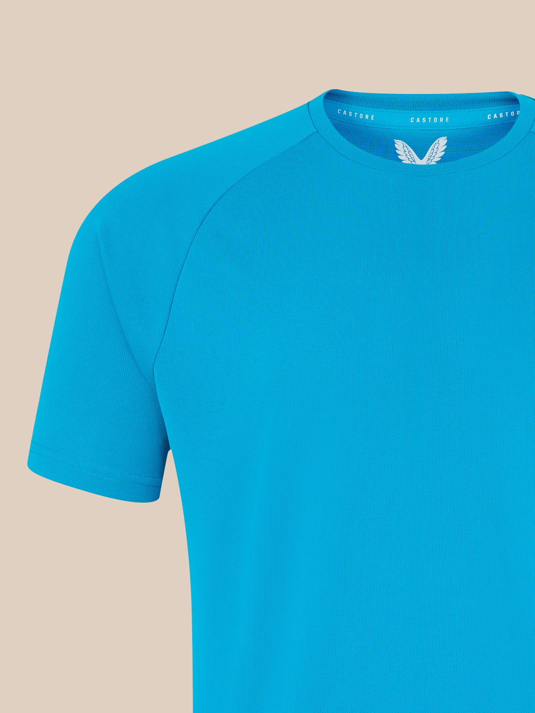 Blue T shirt close up showing shoulder and left chest white wing logo with Castore on the neckline
