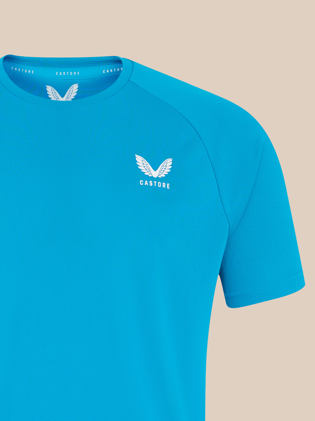 Close up of blue T shirt chest with white wing logo and Castore text on the collar trim