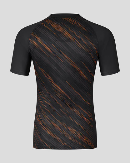 Rear view of Leicester Tigers black warm up jersey with orange diagonal geometric pattern across the back.