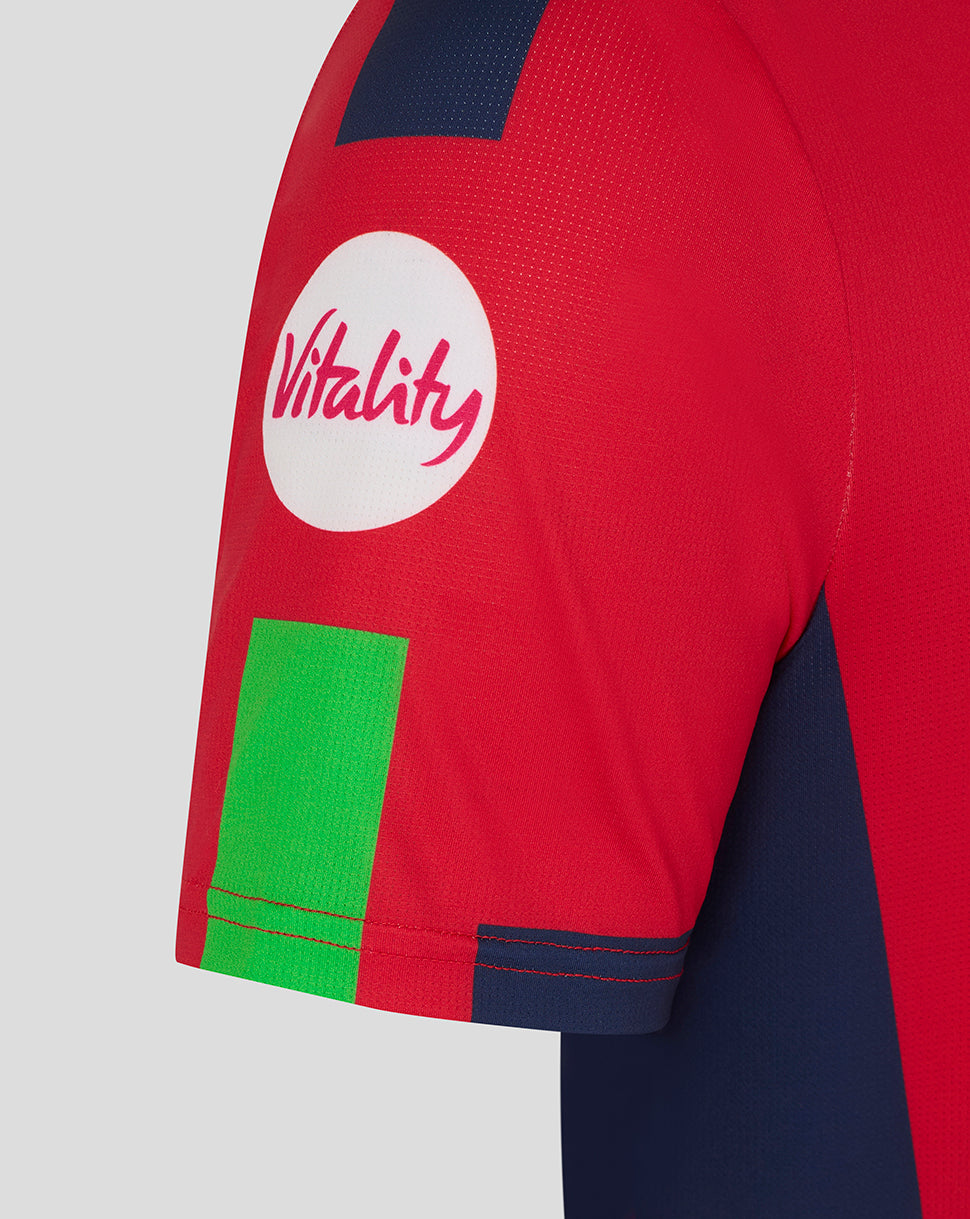 Close-up of red sleeve showing Vitality logo in a white circle and a bright green patch with navy trim.