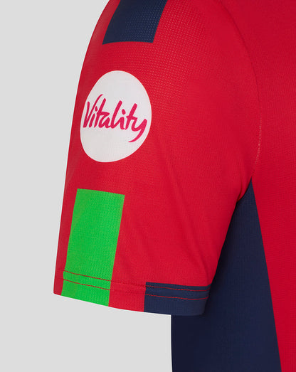 Close-up of red sleeve showing Vitality logo in a white circle and a bright green patch with navy trim.
