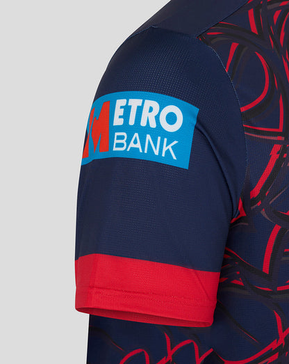 Close-up of the sleeve showing a Metro Bank blue sponsor patch on dark navy fabric with red cuff