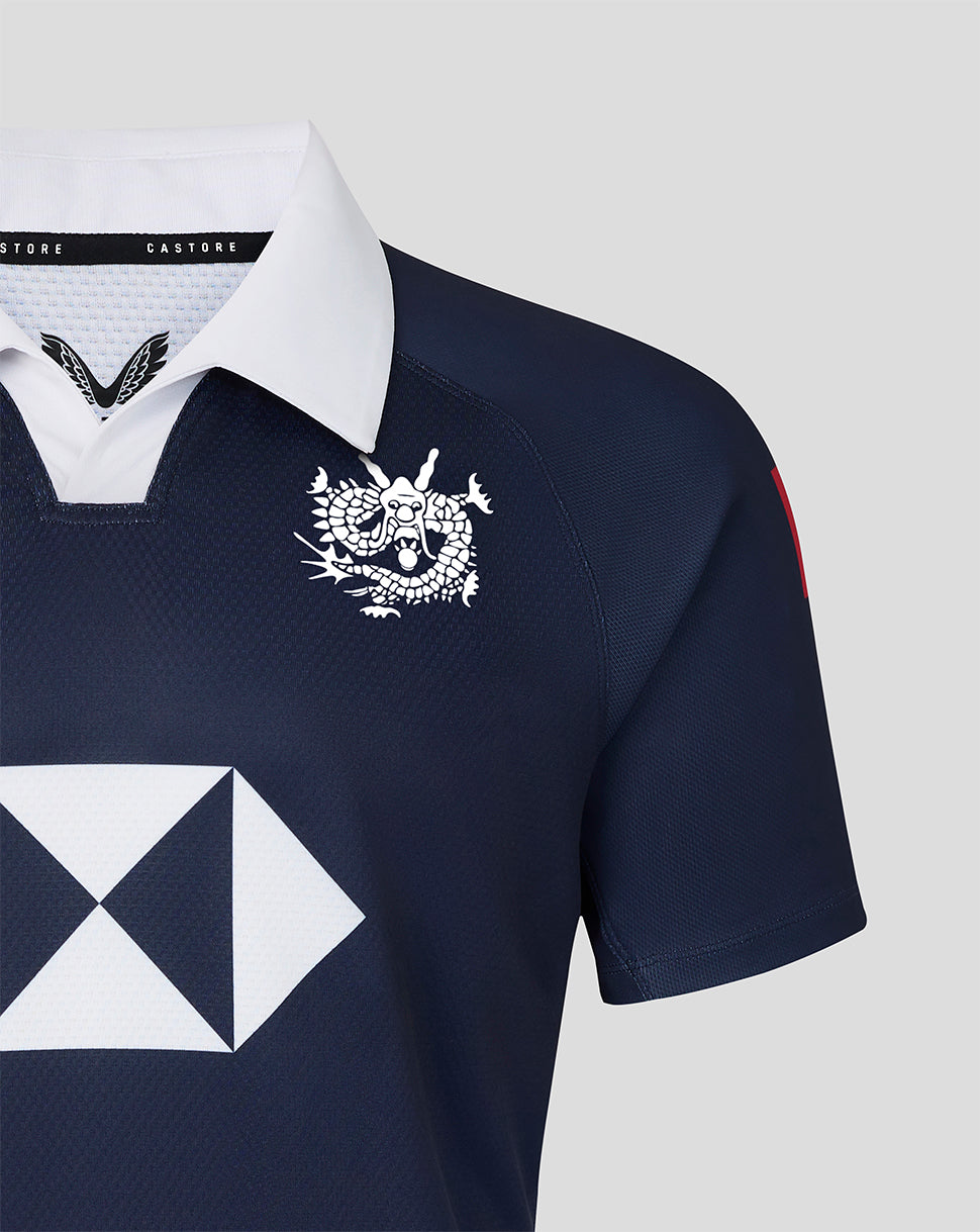 Male model wearing navy HK7s jersey with white collar and dragon crest on chest, holding a white and pink patterned rugby ball