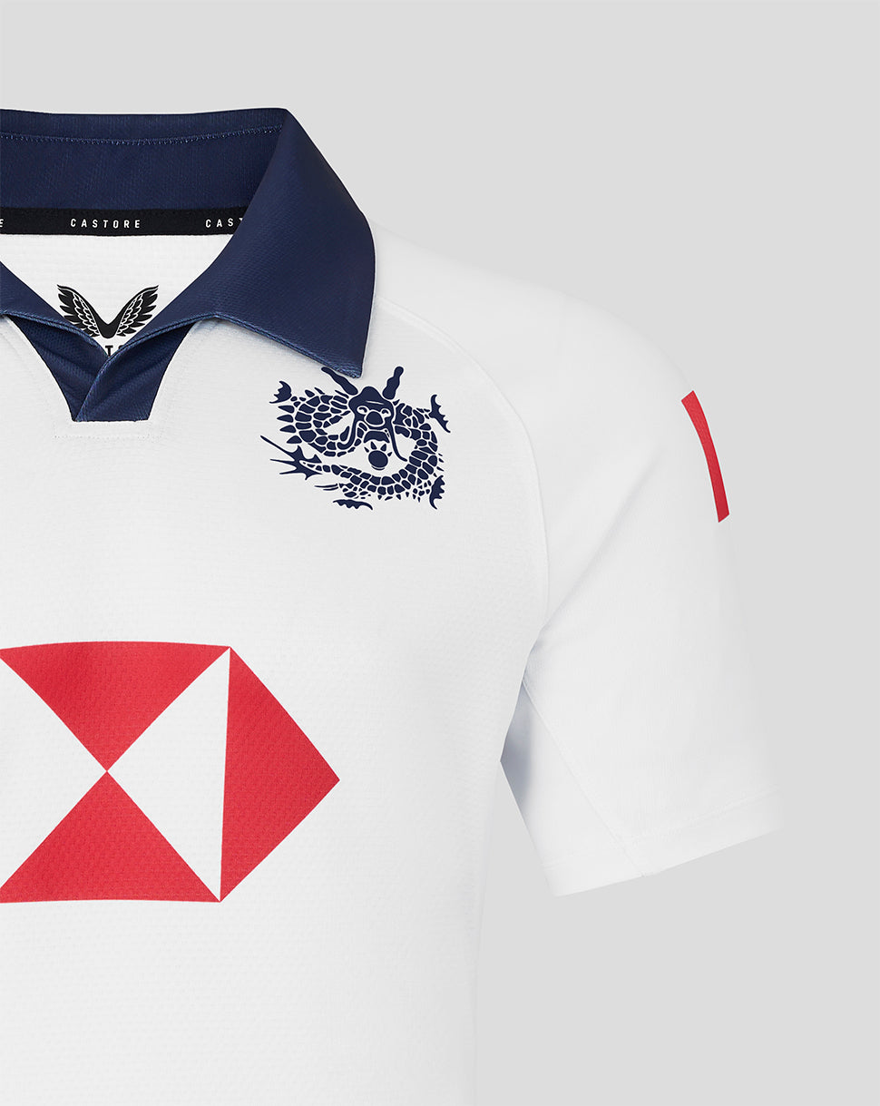 White junior rugby jersey with navy collar, blue dragon crest on the chest and a red diamond sponsor patch