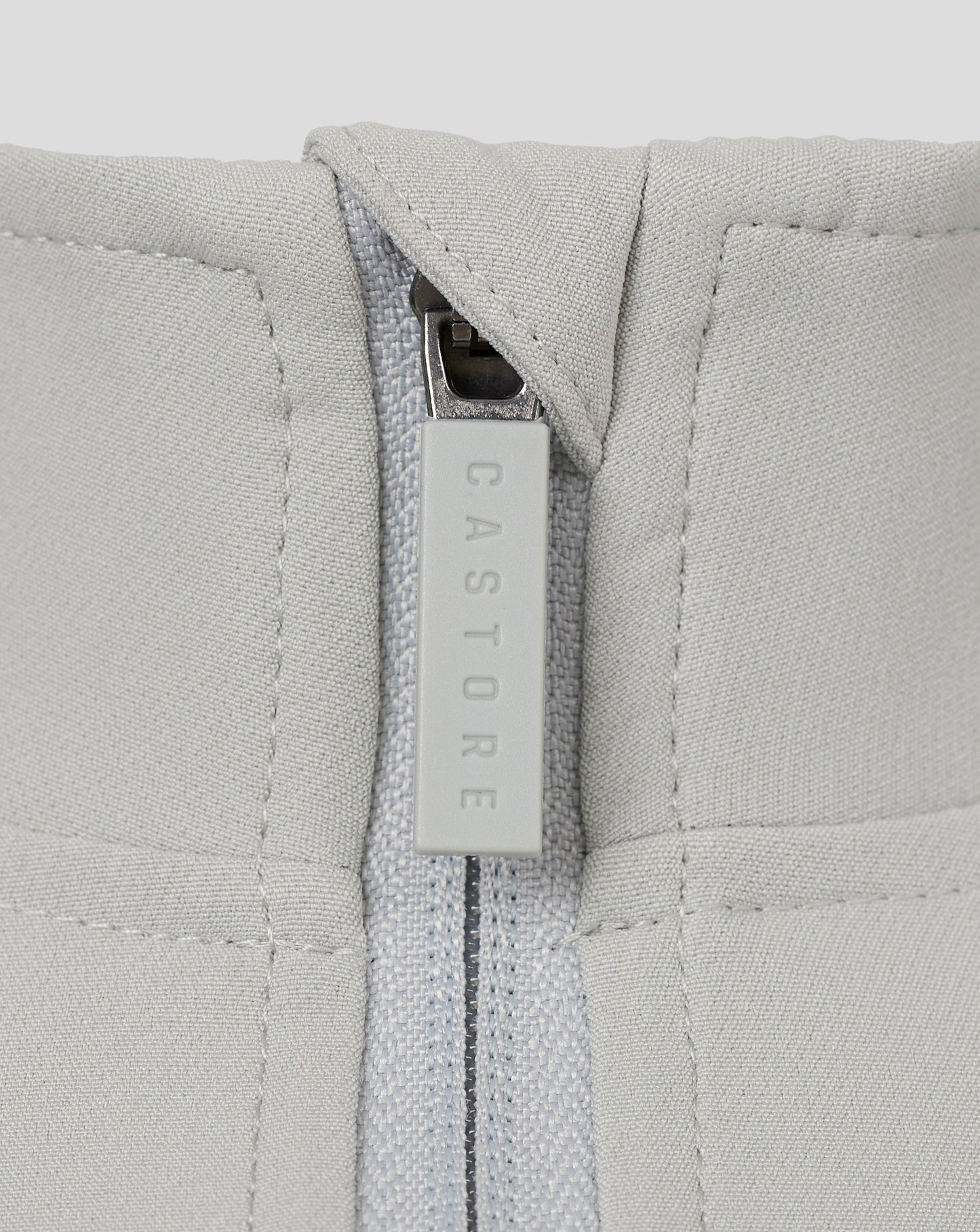 Close-up of light grey track jacket zipper with a CASTORE branded pull.