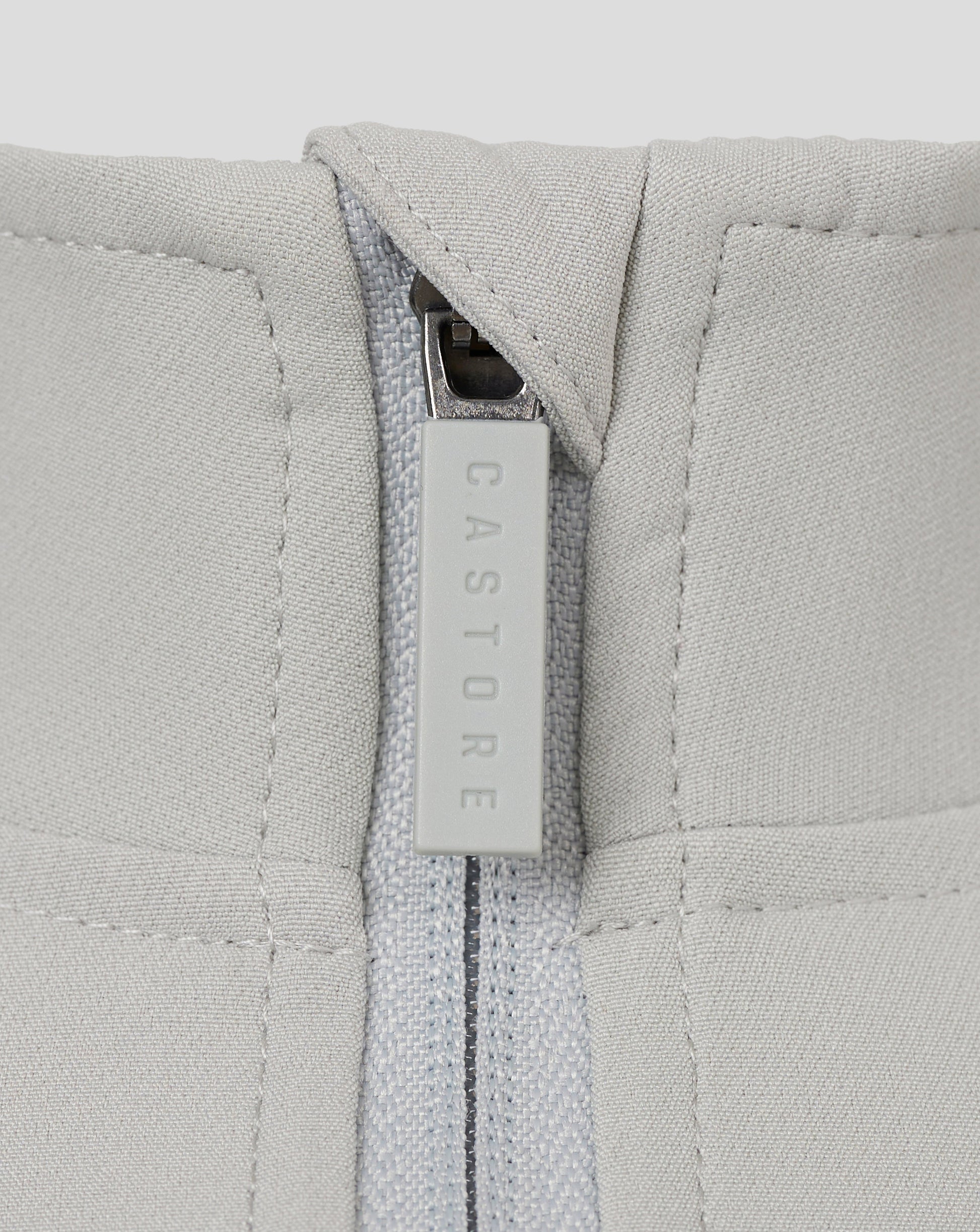 Close-up of light grey track jacket zipper with a CASTORE branded pull.