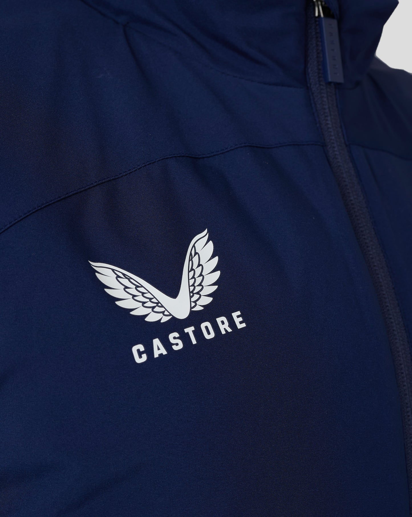 Close-up of navy padded gilet with Castore logo and white wing emblem, featuring the zipper and textured fabric