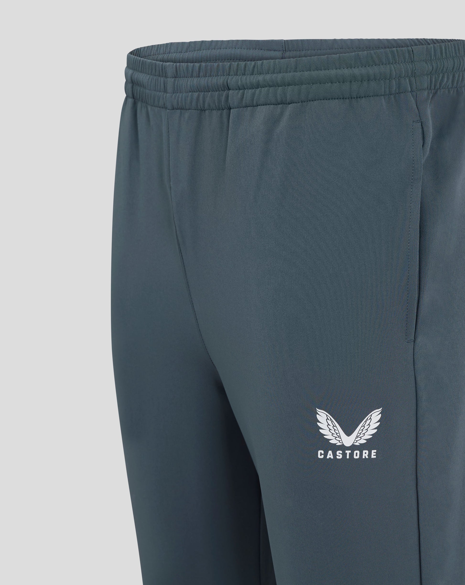 Close up of dark slate mens track pant waist showing elastic waistband with drawcord and Castore logo on the leg