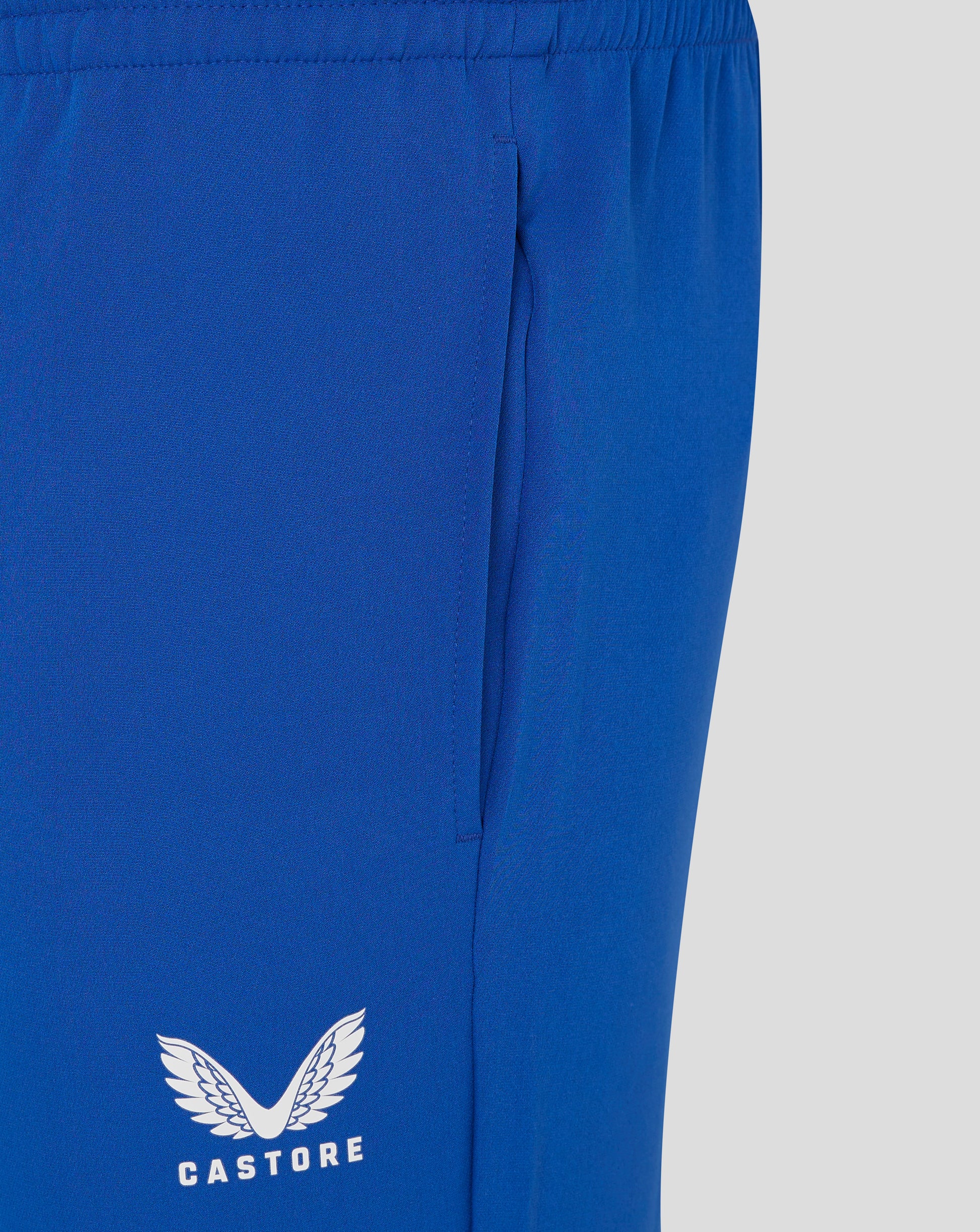 Close-up of royal blue track pants fabric with a white Castore logo featuring wings on the leg.