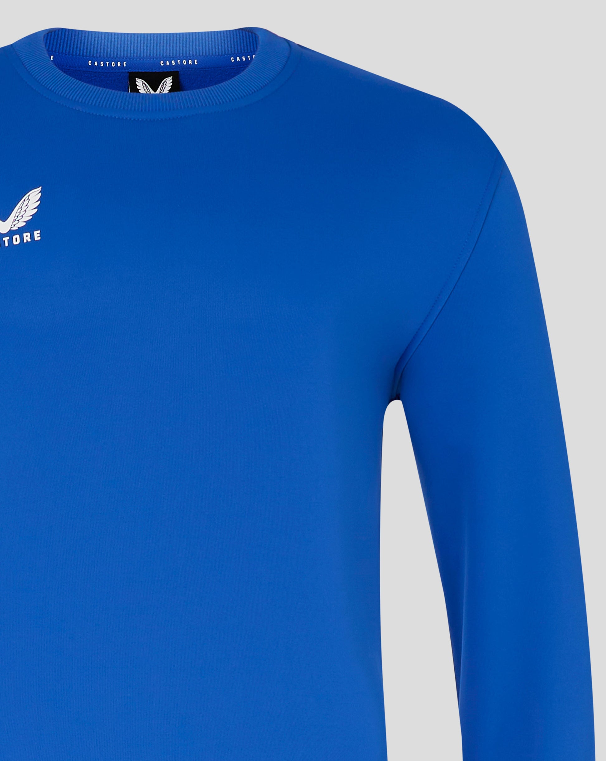Blue brushback sweatshirt close up showing ribbed crew neck and Castore wing logo on left chest.
