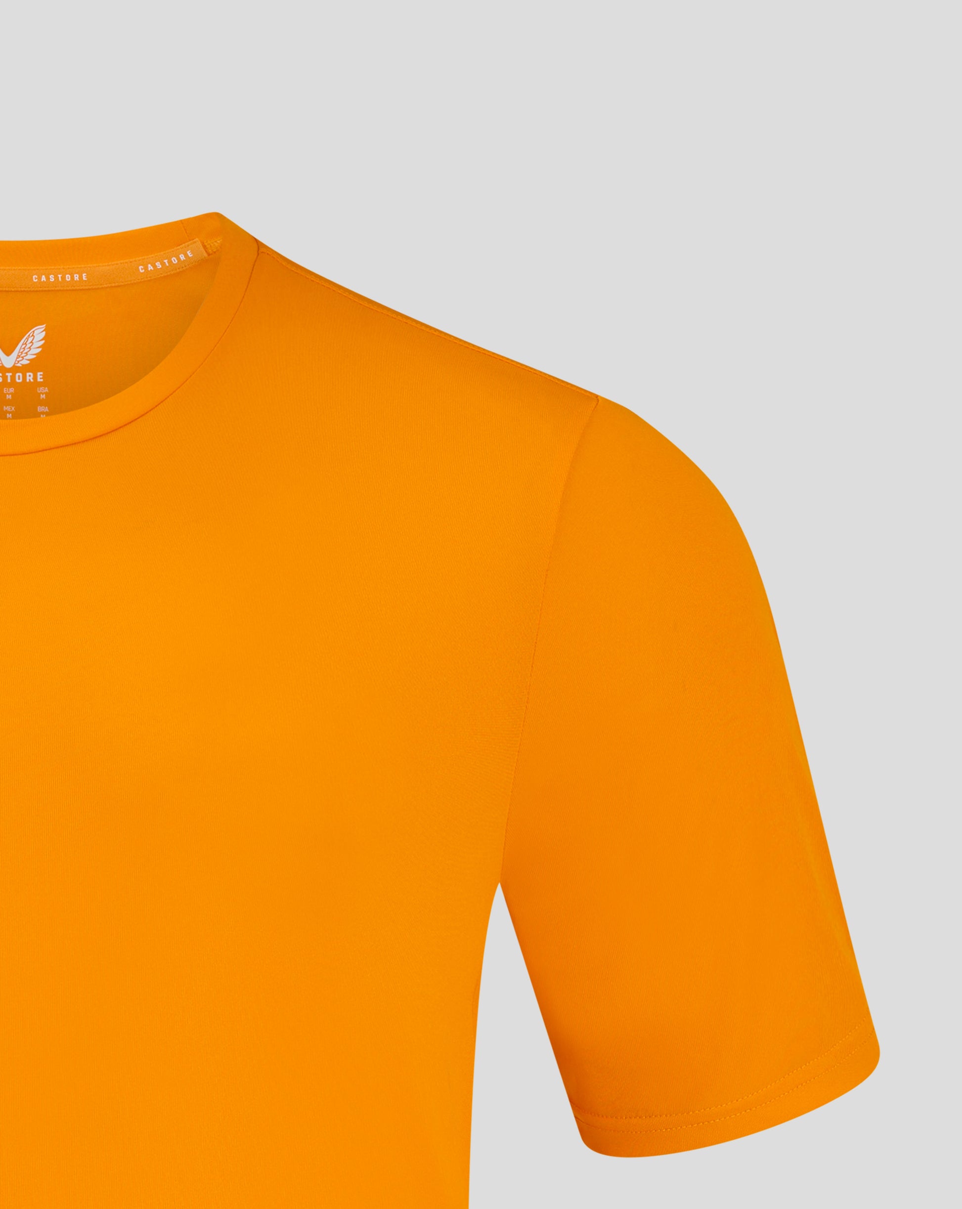 Mens performance tee in bright marigold shown close up at the crew neck with shoulder seam and heat sealed Castore logo