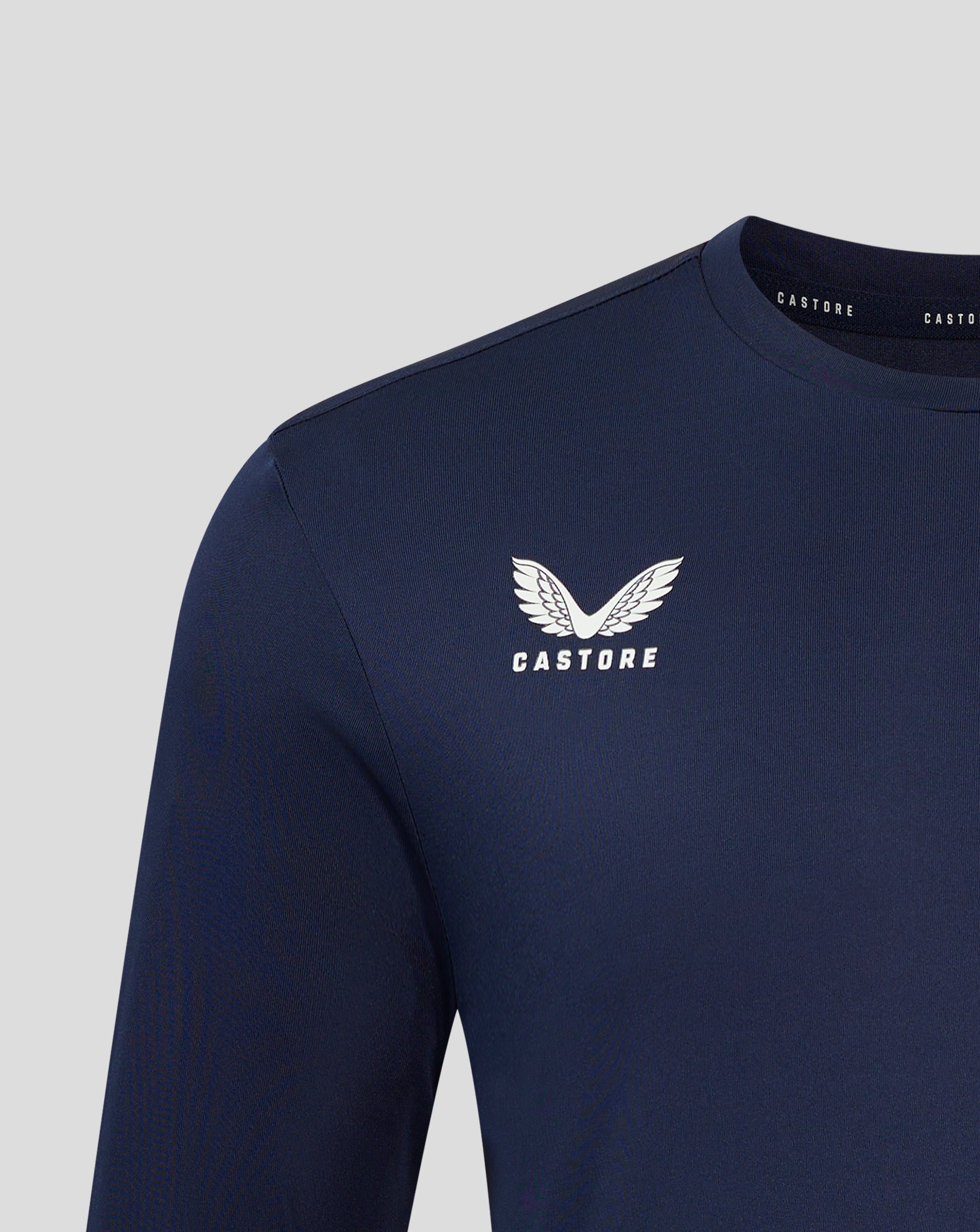 Close up of navy Peacoat long sleeve tee chest area with white Castore logo and wing emblem near the neckline