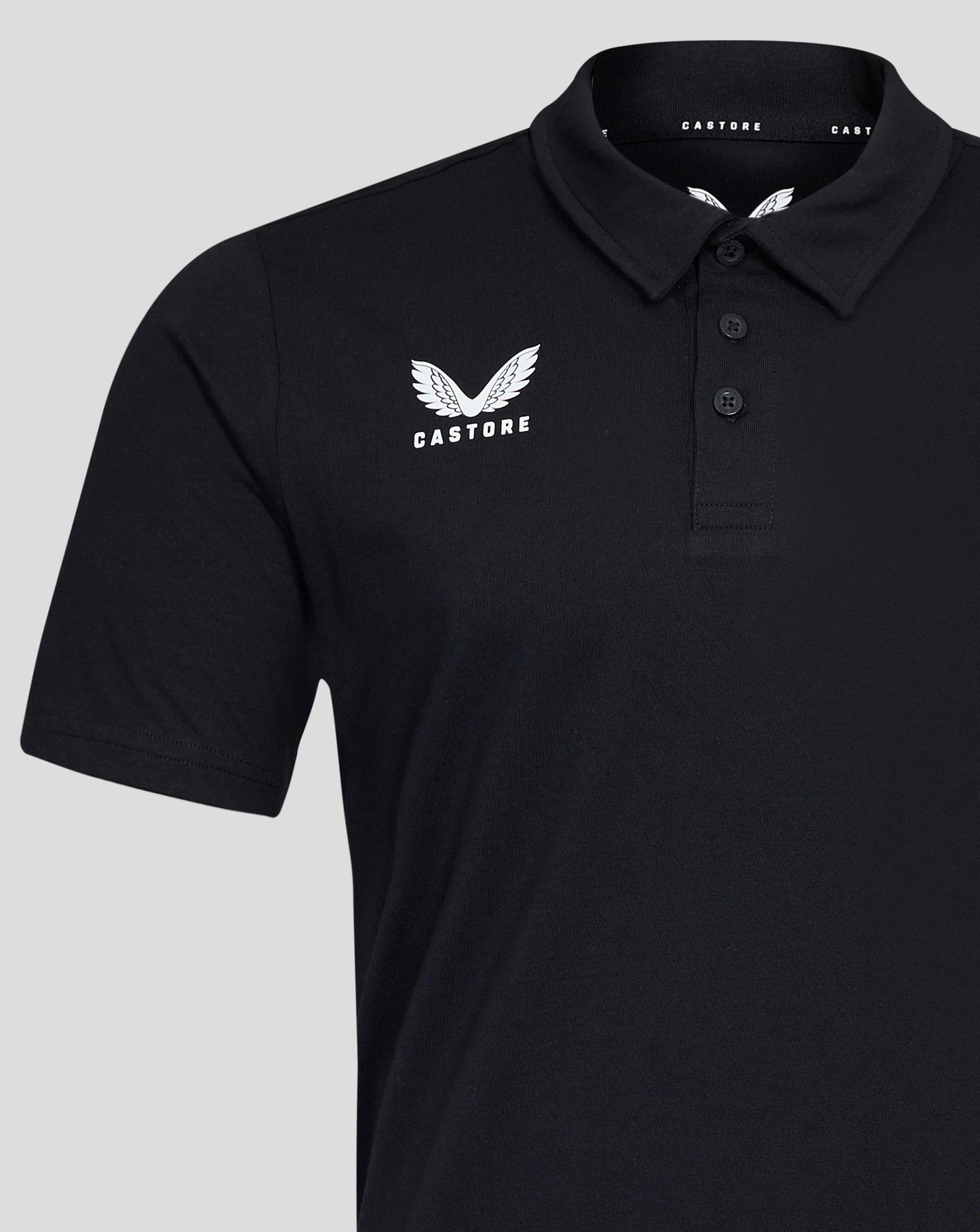 Close-up of the black polo chest showing the white Castore wing logo and the three button placket at the collar