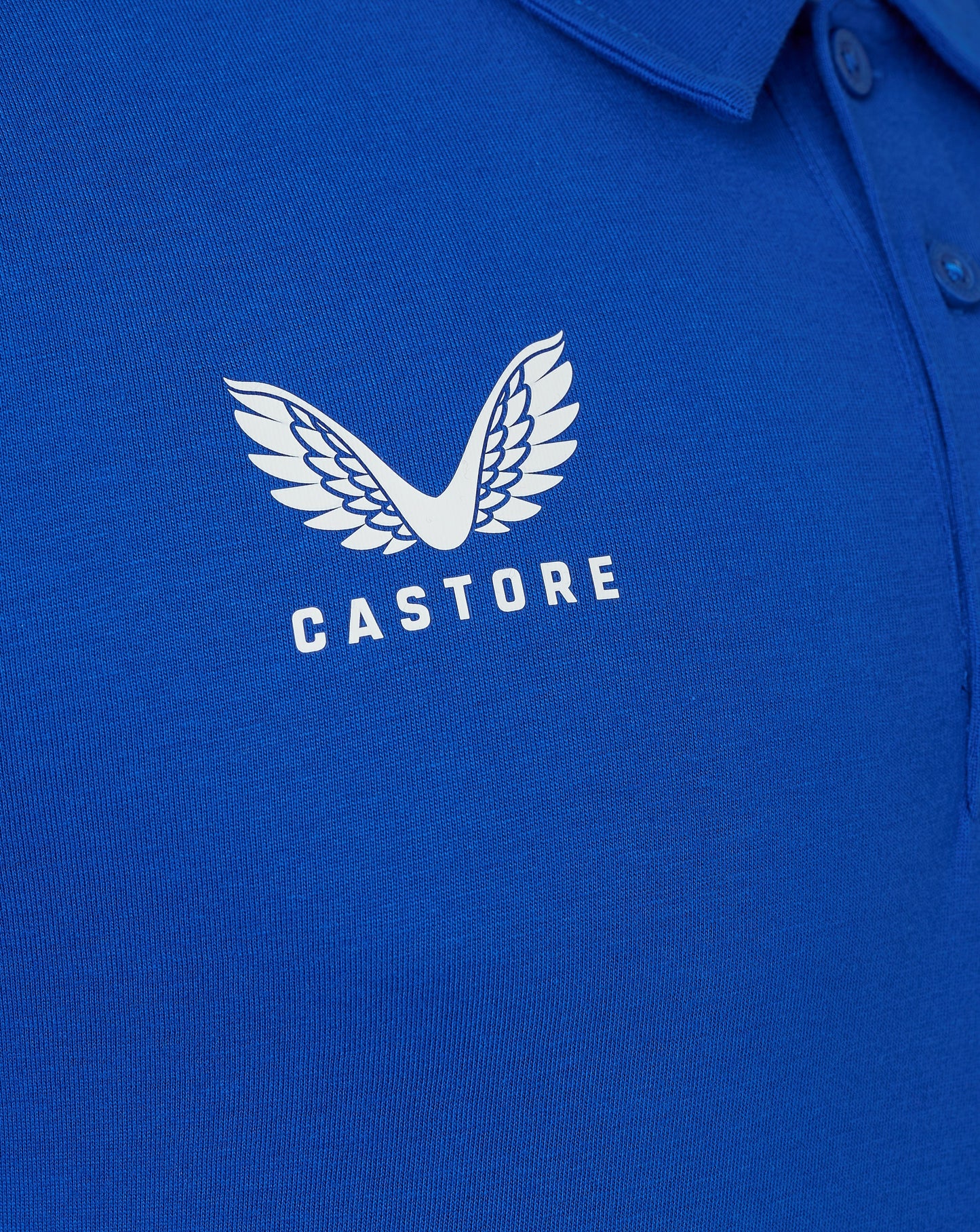Close-up of white Castore wing logo on blue polo fabric with CASTORE text
