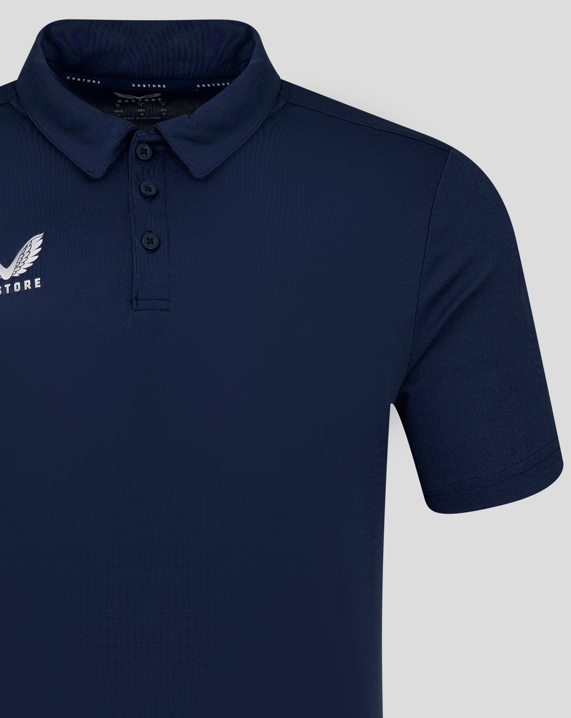 Close up of navy polo showing polo collar and three button placket with Castore logo on left chest.