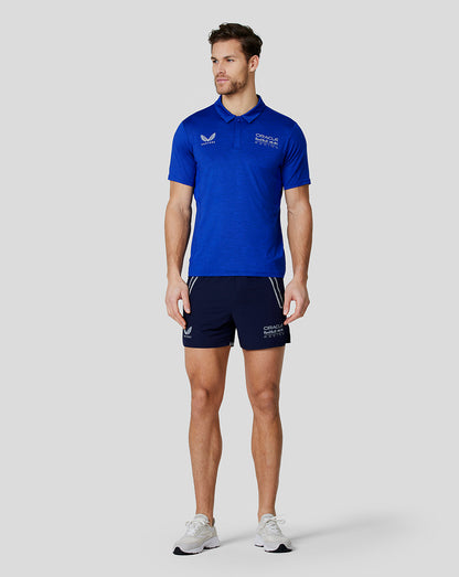 Full body of a man in the blue Oracle Red Bull Racing polo with navy shorts and white sneakers