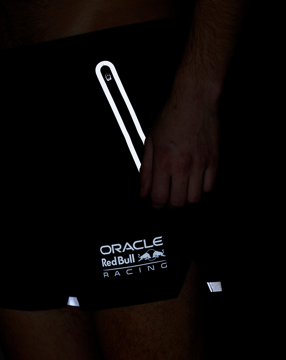 Close-up of black running shorts showing a vertical reflective stripe and Oracle Red Bull Racing logo on the hem
