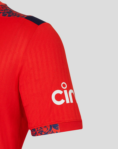 Close-up of red England cricket shirt sleeve showing navy floral shoulder trim.