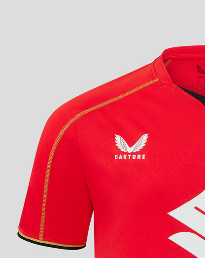 Close up of red Mk Dons jersey shoulder with Castore logo and golden piping along the seam.
