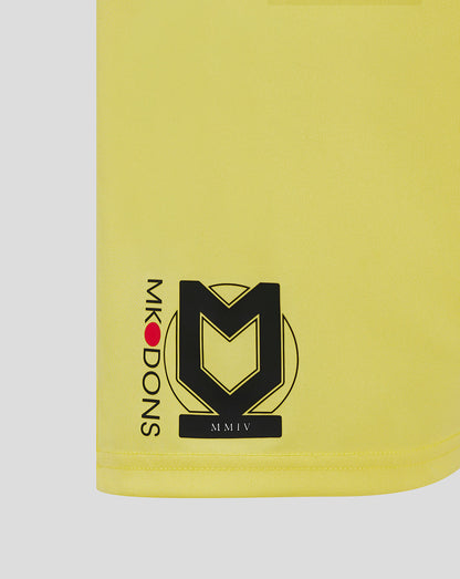 Close-up of lower left leg of yellow MK Dons shorts showing the club crest and MMIV marking