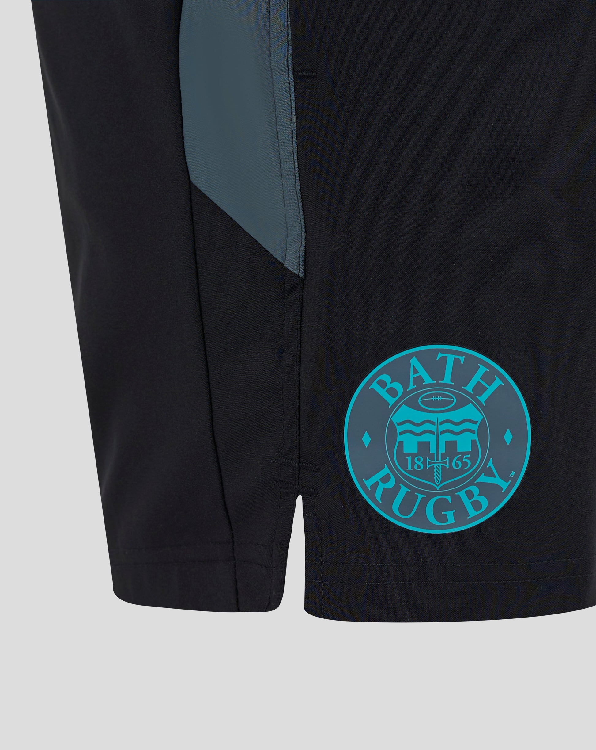 Close up of black Bath Rugby shorts with teal side panel and turquoise circular Bath Rugby crest on the thigh.
