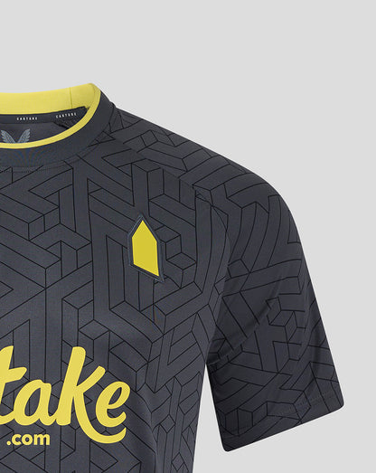 Close-up of the chest area showing the yellow crest and partial Stake sponsor on the dark geometric fabric