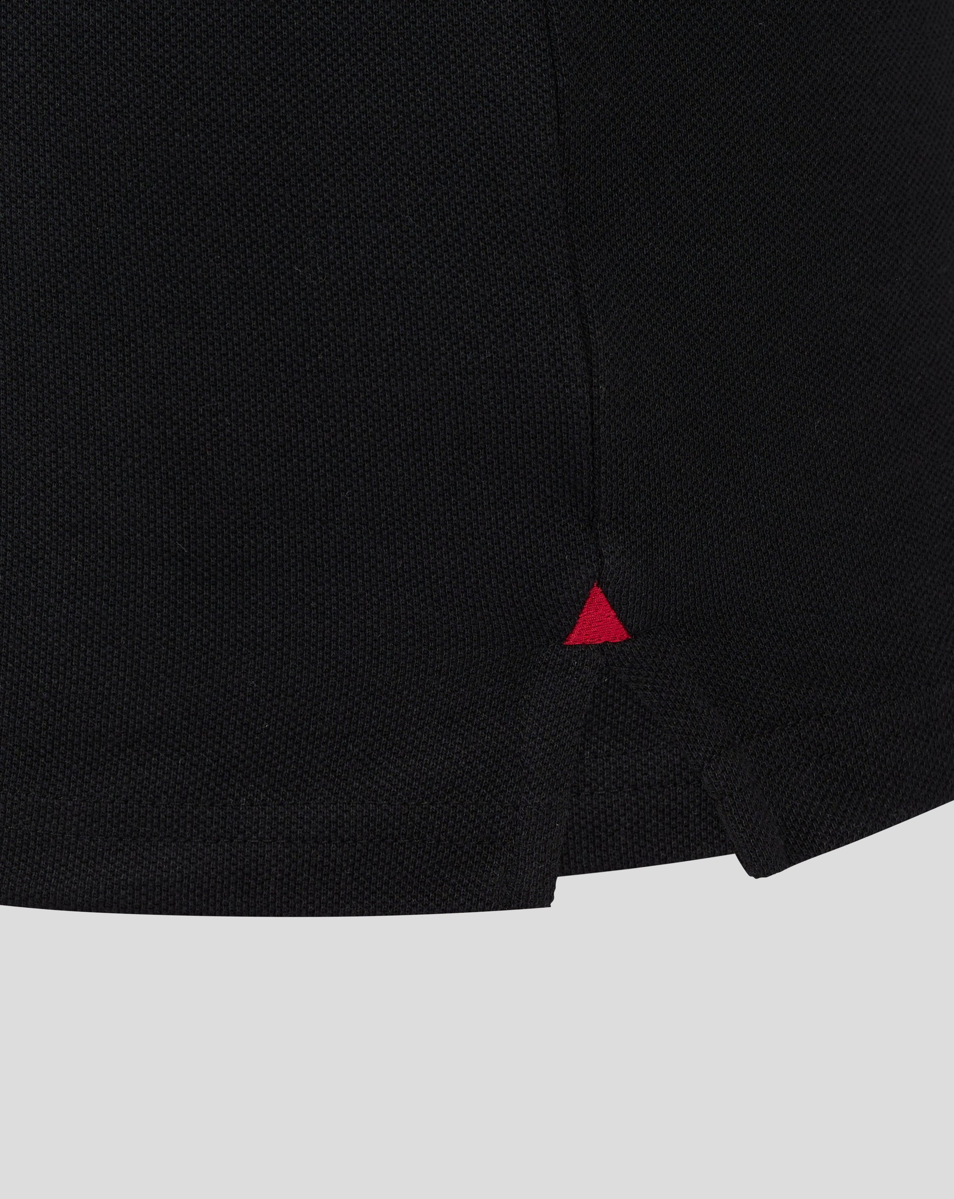 Close-up of black Rangers polo fabric showing textured knit and a small red triangle logo