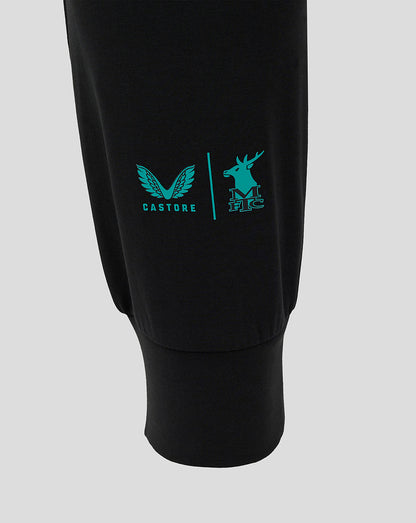 Close up of the left leg showing turquoise Castore wing logo and Mansfield Town crest on black fabric.