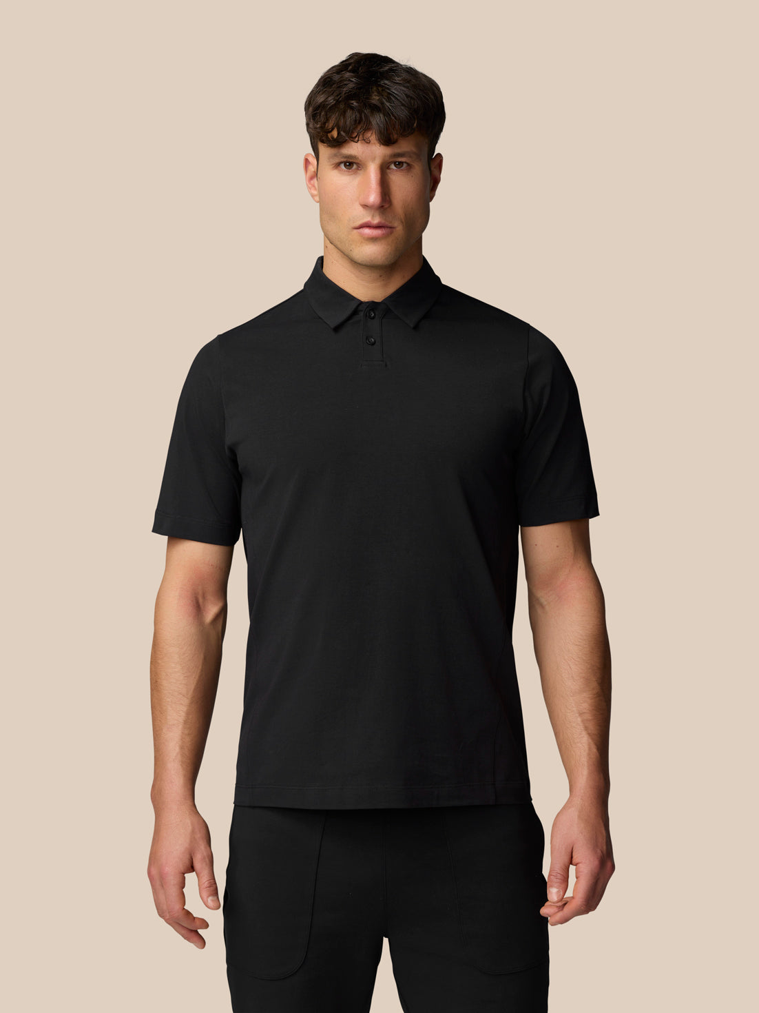 Male model wearing black Travel Polo shirt photographed against a beige background