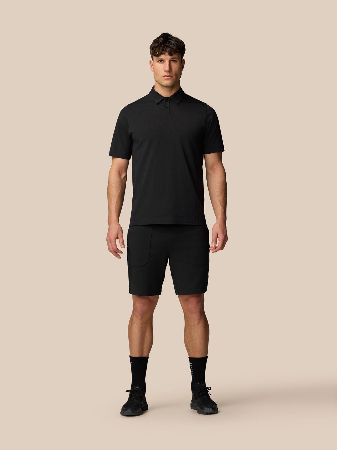 Male model wearing black Travel Polo with matching black shorts.